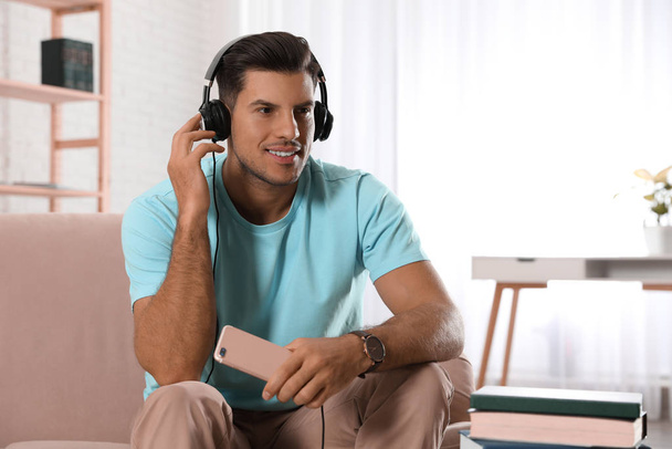 Uomo con cellulare che ascolta audiolibro sul divano in casa
 - Foto, immagini
