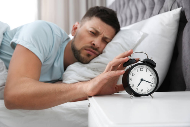 Sleepy man turning off alarm clock at home in morning, focus on  - Valokuva, kuva