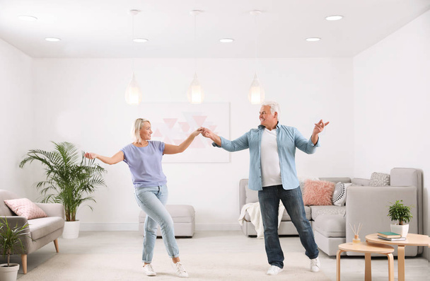 Happy mature couple dancing together in living room - Fotó, kép
