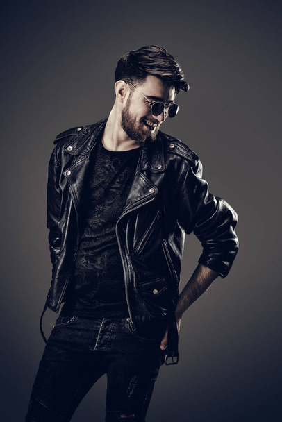 Young Hipster in Leather Jacket, Smiles, Head Leaning to the Side - 写真・画像