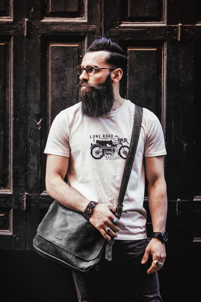Portrait of a young hipster in front of a black wooden door - Foto, Imagen