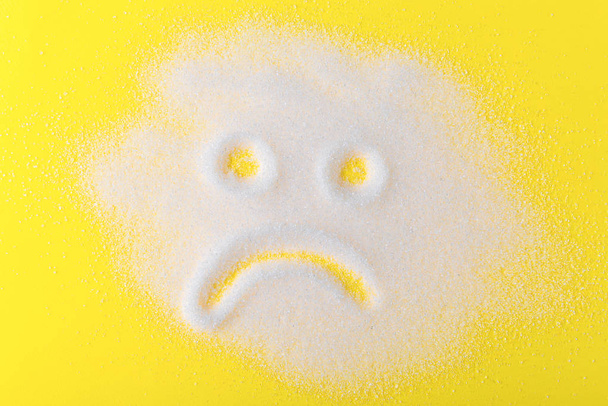 Sůl roztroušená po černém povrchu. Nakreslený smutný obličej. Koncepce - strava, poškození zdraví v důsledku nadměrné konzumace soli a cukru. - Fotografie, Obrázek