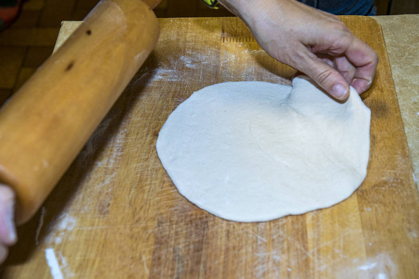 Ciasto pizzowe okrągłe jest zwijane z mąką i deską drewnianą - Zdjęcie, obraz