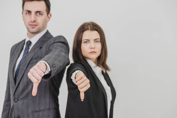 Business man and woman standing back to back, giving thumbs down, frowning. Focus on the gesture on the forefront. - Фото, изображение