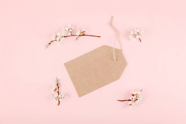 Minimalistic card mockup with empty recycled craft cardboard, blossom cherry flower branch on pink background. Flat lay, top view, copy space - Fotó, kép