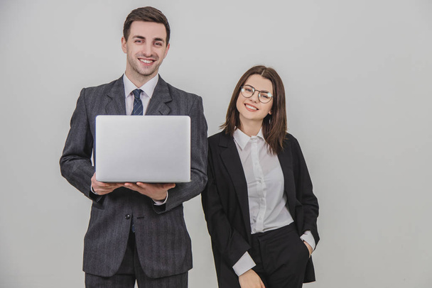 Business couple. Man holding laptop, woman standing by his side putting hand in the pocket. - Foto, immagini