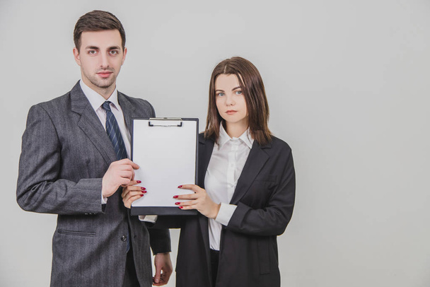 Successful business couple standing with confident face expressions, holding together a clipboard with empty clear sheet of paper for text. - Zdjęcie, obraz