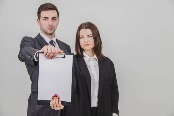 Blurred successful business couple standing with confident face expressions, extending to the camera a clipboard with empty clear sheet of paper for text. - Photo, Image