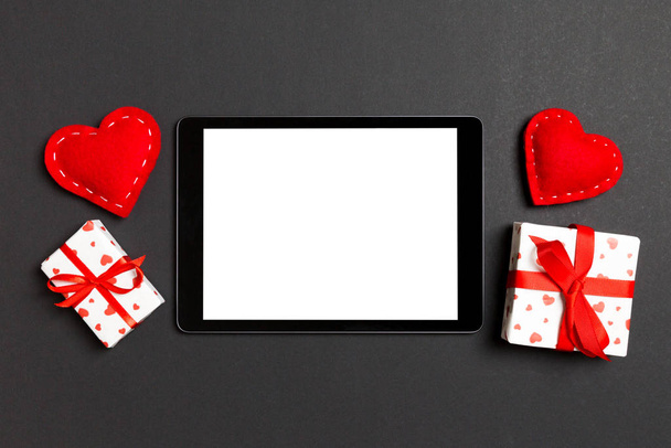Вид сверху на цифровой стол, окруженный подарочными коробками и сердцами на цветном фоне. День Святого Валентина - Фото, изображение