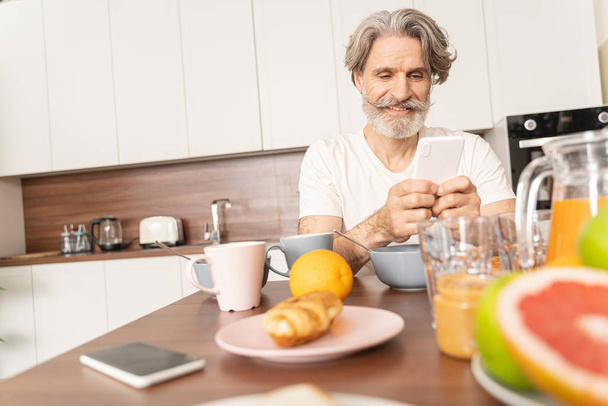 Pleased man using his smartphone at breakfast - Foto, Bild
