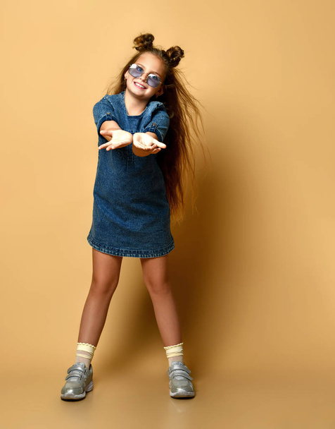 Cute girl in jeans sundress and sunglasses posing on camera. - Foto, afbeelding