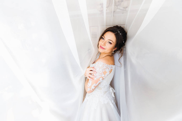 Красива наречена в білій сукні дивиться на камеру і посміхається під кутом
 - Фото, зображення