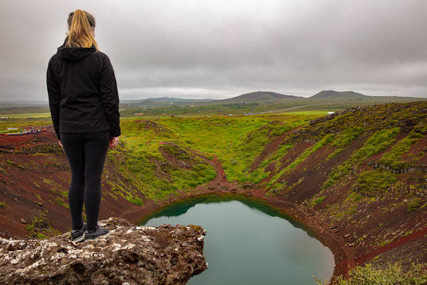 Blonde Forscherin steht auf Felsen und blickt auf den Kerid-Kratersee - Foto, Bild