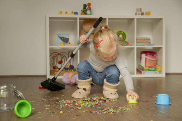 Küçük tatlı sarışın kız süpürgeyle oynuyor, yerden renkli konfeti temizliyor. - Fotoğraf, Görsel