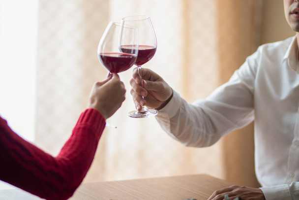 A cheerful young couple crossing their wineglasses at a restaurant. A man and his girlfriend drinking wine at a cafe. Red rose on a table. Valentine's day concept. - Foto, afbeelding