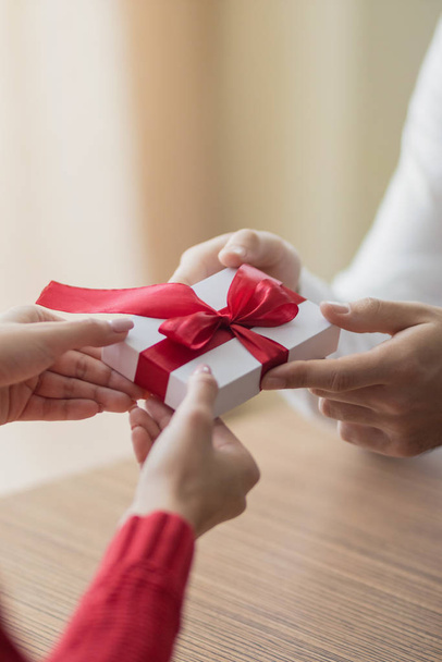 A small present is being passed by a couple from one to another. White little giftbox with a red ribbon in the hands. Valentine's day and winter holidays concept. - Fotografie, Obrázek