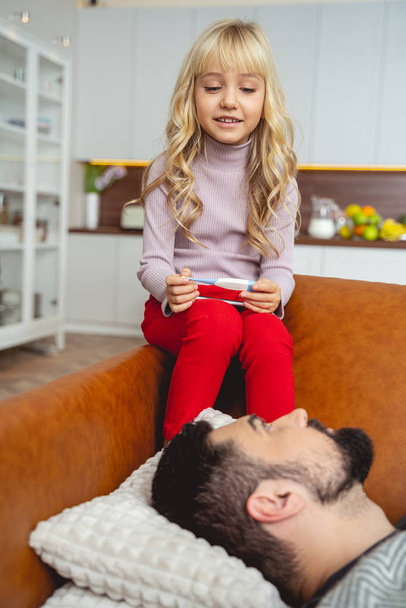 Little girl with thermometer sitting beside her sick father - Photo, image