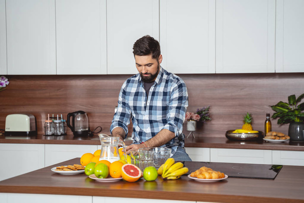 Handsome bearded man making breakfast in kitchen - Photo, Image