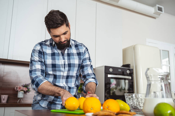 Attractive young man cutting orange in kitchen - Photo, image