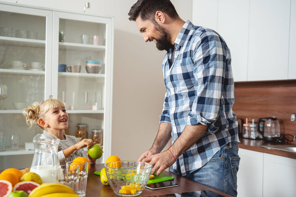 Cheerful young man cooking fruit salad with daughter - Photo, image