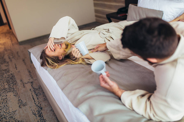 Couple in bathrobes lying on bed in hotel room. - Valokuva, kuva