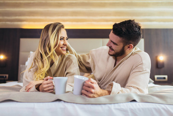 Couple in bathrobes lying on bed in hotel room. - Фото, зображення