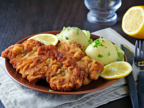 Wiener Schnitzel mit Kartoffelsalat serviert mit Zitronenscheiben und Petersilienblättern - Foto, Bild