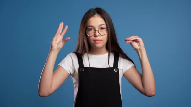 Cute woman in glasses showing bla-bla-bla gesture with hands and rolling eyes isolated on blue background. Empty promises, blah concept. Lier. - Video, Çekim