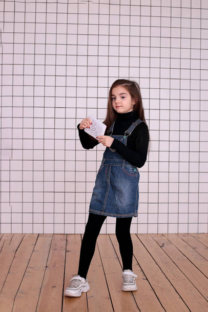 молода добра грайлива дівчина восьми років з довгим волоссям в чорному черепашці і джинсовий сарафан зі знаком "Так
" - Фото, зображення