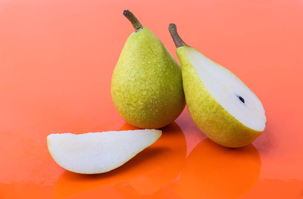 Tasty wet pears on an orange background - A pear cut in half, a piece and a whole pear - Foto, imagen