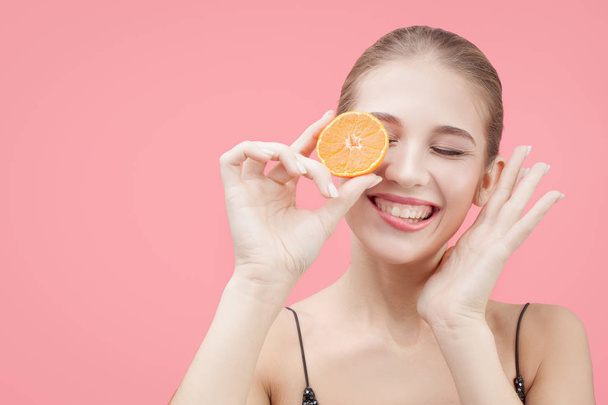 happy woman with an orange in her hands. Pink background - Foto, imagen