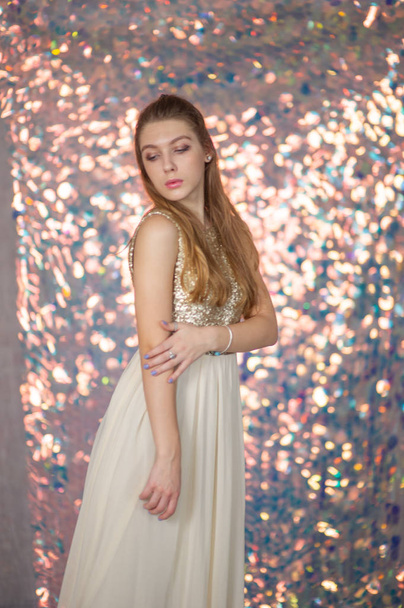 Beauty portrait of a beautiful girl with a silver shiny dress with evening make-up on a background of Christmas lights. - Photo, Image