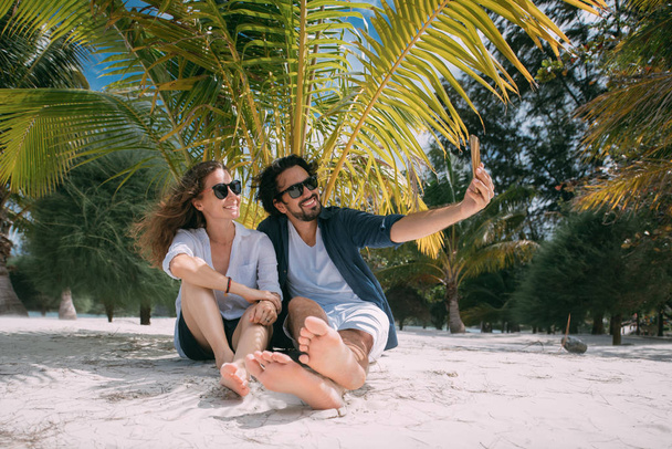 A pair of lovers take a selfie under a palm tree on a tropical beach - Foto, immagini
