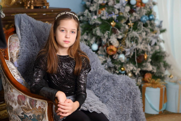 Beautiful girl in a chair on the background of the Christmas tree - Fotografie, Obrázek
