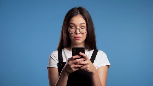 Asian young girl sms texting, using app on smartphone. Pretty woman surfing internet with mobile phone. Blue studio footage. - Materiał filmowy, wideo