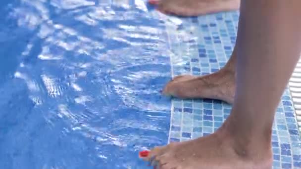Two pairs of female legs stand on the side of the pool with blue clear water and move their fingers. - Filmagem, Vídeo