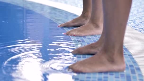 Two pairs of female legs stand on the side of the pool with blue clear water and move their fingers. - Imágenes, Vídeo
