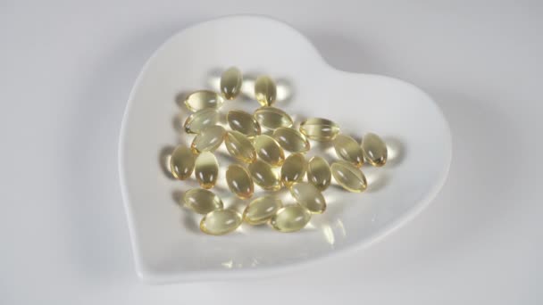 Een man voegt meerdere gele medische capsules toe aan een stapel op een witte plaat in de vorm van een hart op een witte tafel. Voedingssupplementen voor de behandeling van ziekten en verbetering van de immuniteit - Video