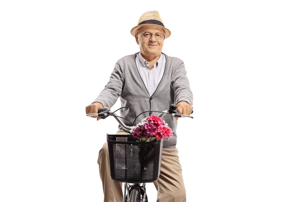 Elderly man riding a bicycle with flowers in basket  - Zdjęcie, obraz