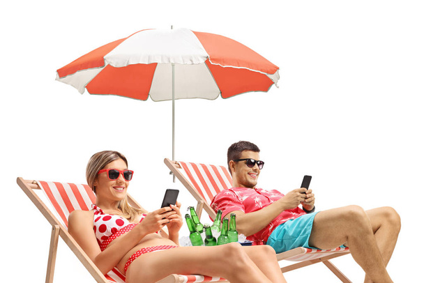 Young man and woman with phones sunbathing in deck chairs - Фото, изображение