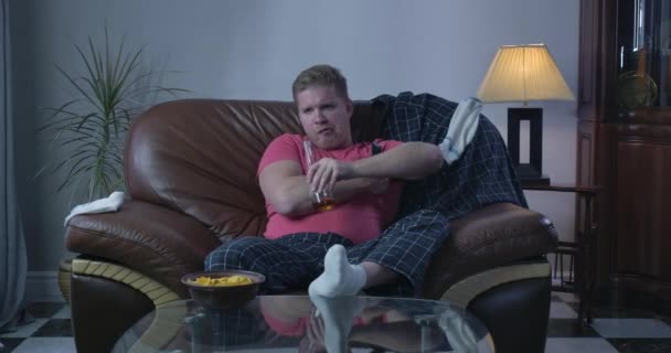 Adult redhead Caucasian man drinking beer and switching channels. Single guy watching TV alone on coach. Addiction, loneliness, alcoholism. Cinema 4k ProRes HQ. - Záběry, video