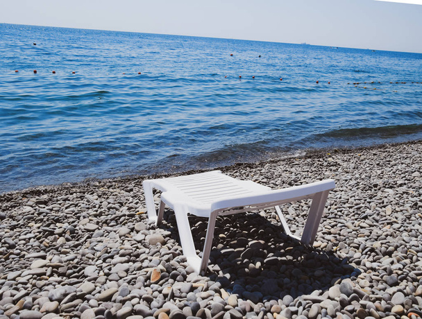 Chaise lounge is white on a stony beach by the coastline. Chaise lounge by the sea - Photo, Image