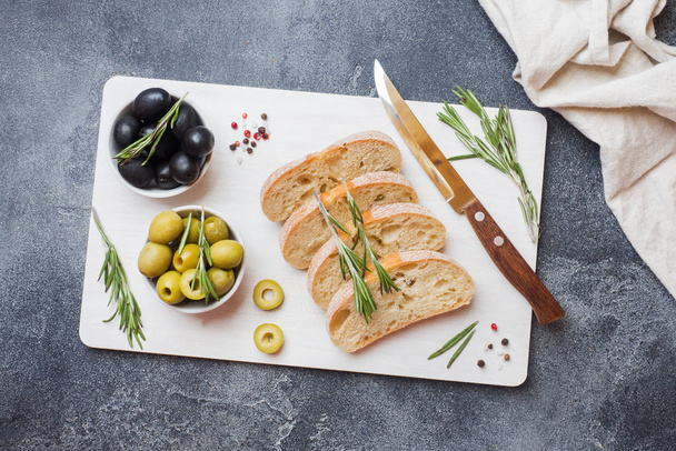 Italian ciabatta bread with olives and rosemary on a cutting Board. Dark concrete background. Copy space. - Fotó, kép