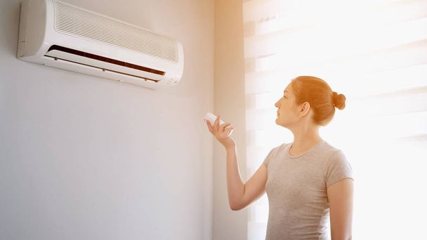 Nuori nainen kytkee ilmastointilaitteen kaukosäätimestä
. - Valokuva, kuva