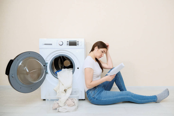 Ev hanımı yeni çamaşır makinesi ayarlarını yerde öğreniyor. - Fotoğraf, Görsel