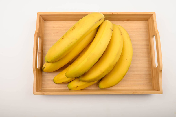 Um monte de bananas amarelas maduras em uma bandeja de madeira em um fundo branco. Fechar
. - Foto, Imagem