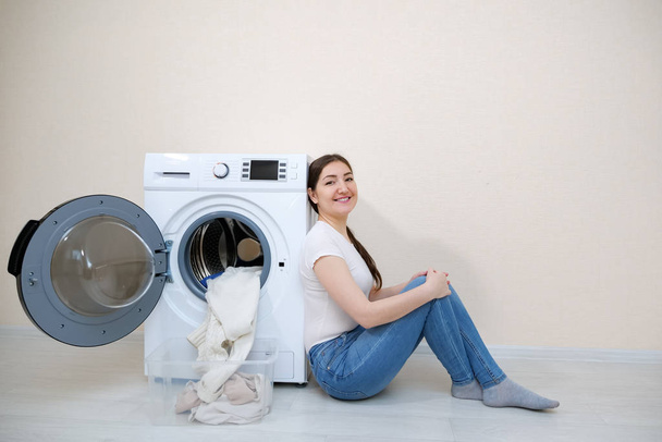 femme assise près de la machine à laver avec blanchisserie propre
 - Photo, image