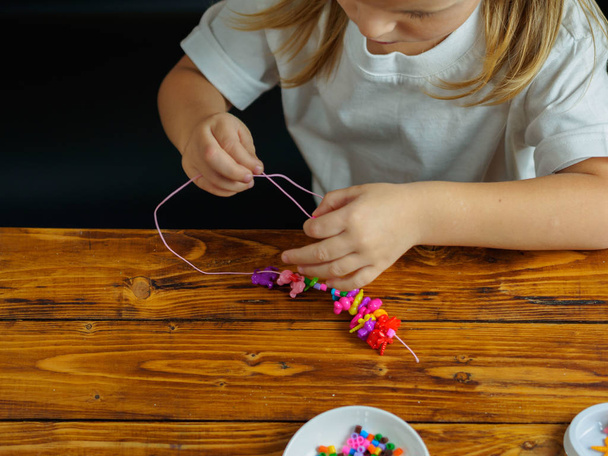 niedliche kleine Mädchen machen ein Armband aus Perlen - Foto, Bild