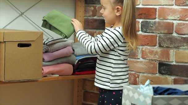 Το κοριτσάκι τυλίγει τα ρούχα σε ένα χαρτόκουτο στο σπίτι. - Πλάνα, βίντεο