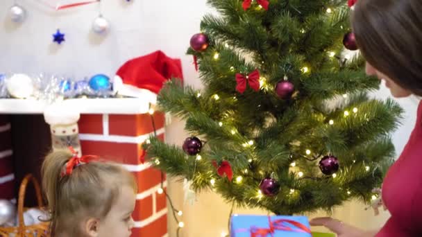 baby and pregnan mom hang red ball toy on Christmas tree. happy childhood concept. child and mother decorate tree with christmas balls. small child and a parent are playing by Christmas tree. - Кадры, видео